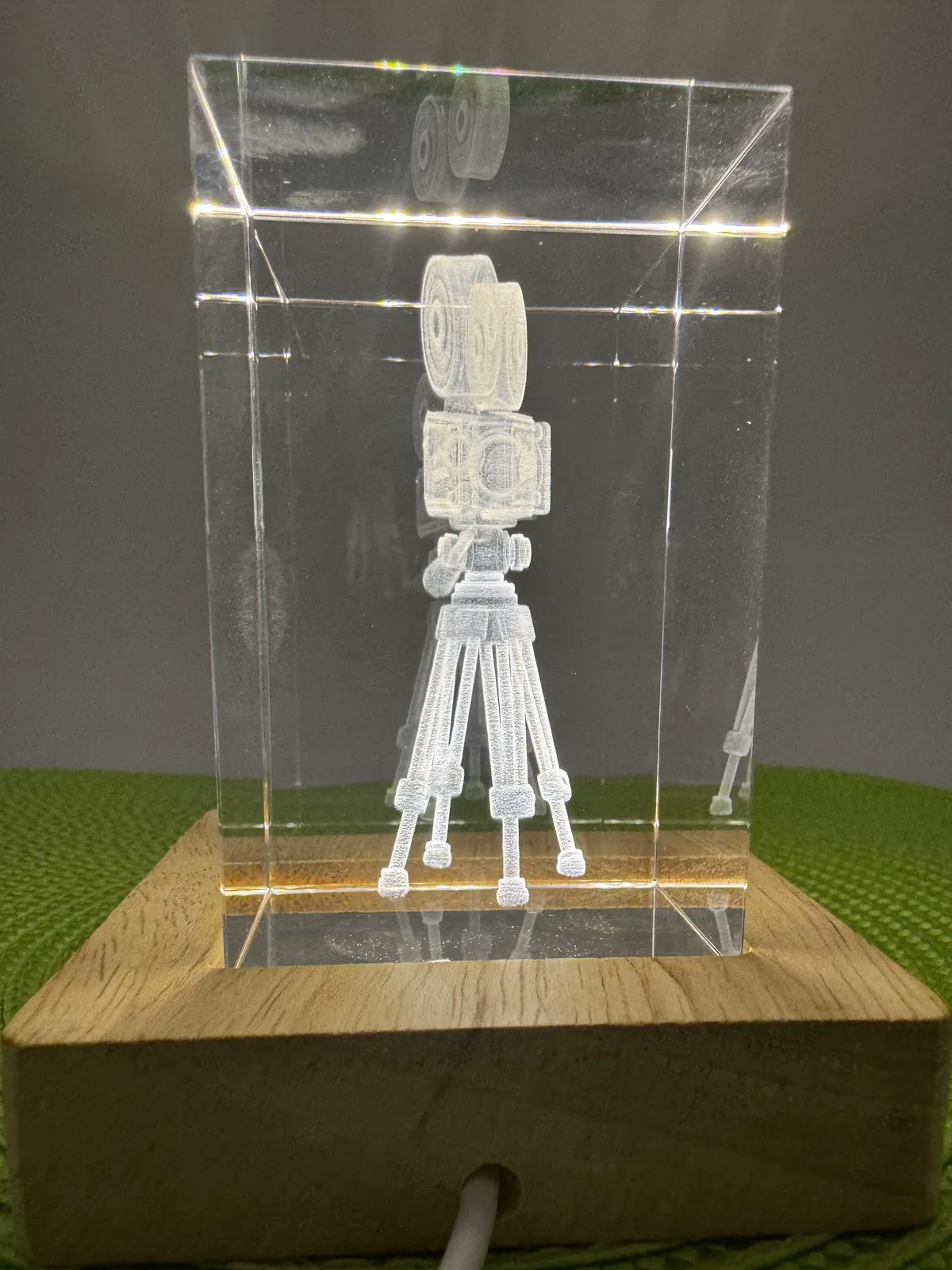 3D-Innengravur einer Filmkamera in einem Kristallblock auf beleuchtetem Holzsockel