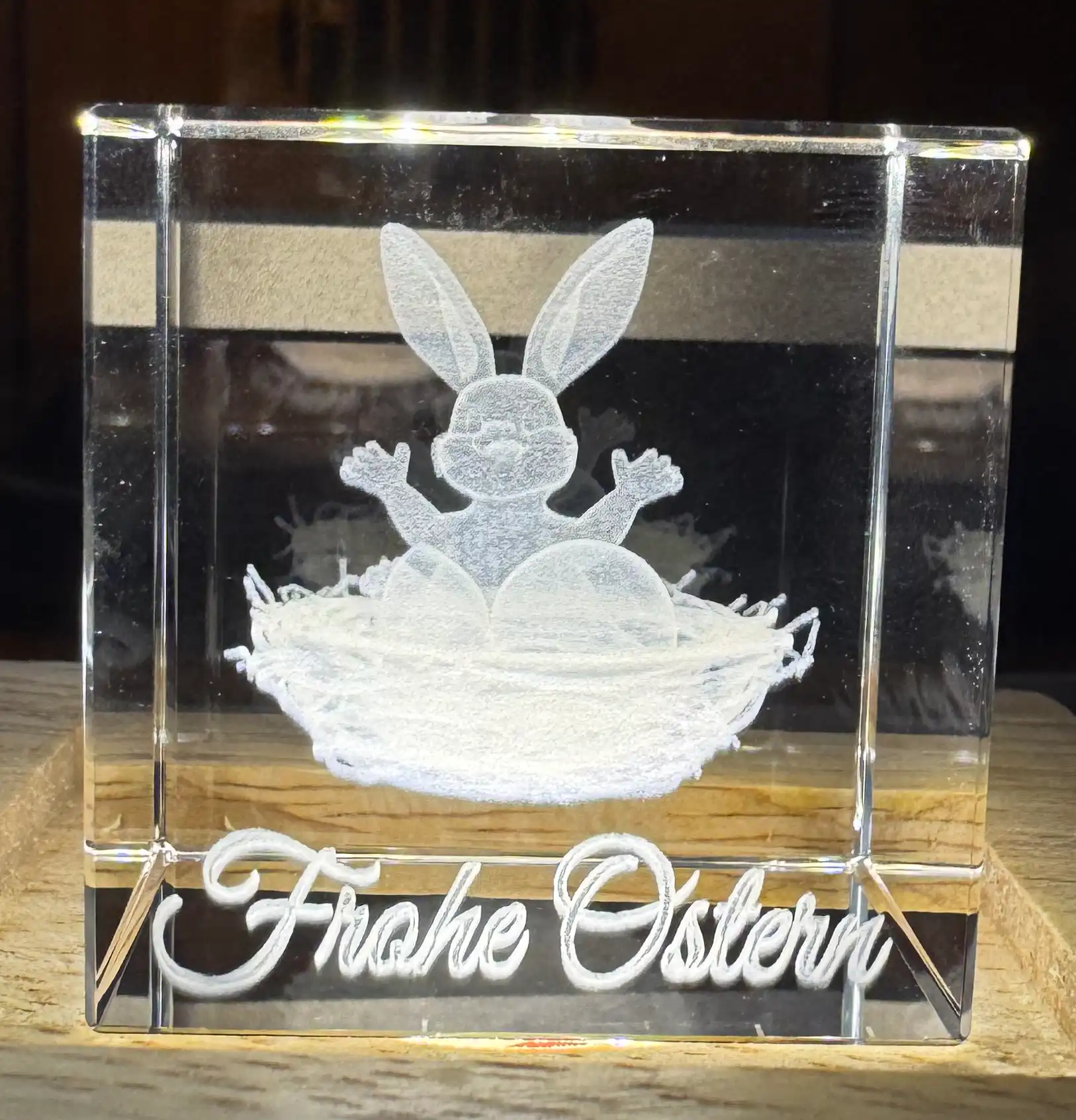 3D-Innengravur eines Osterhasen im Nest mit Schriftzug »Frohe Ostern« in einem Kristallwürfel auf Holzsockel
